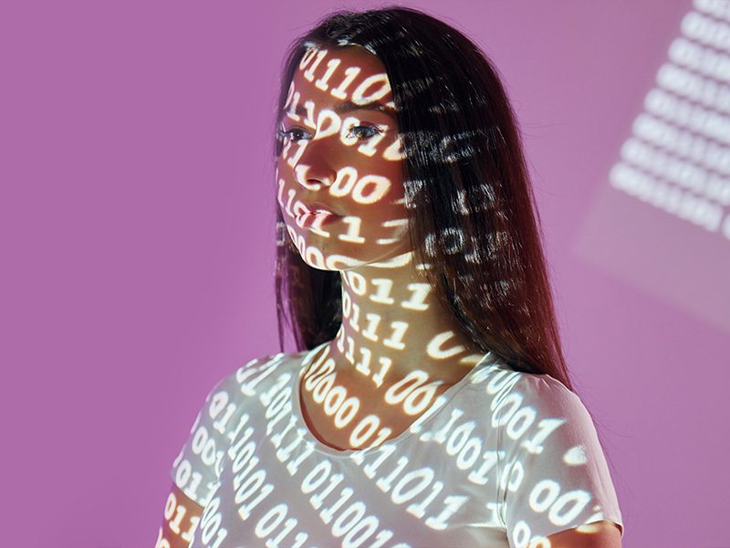 una chica con el rostro cubierto por una proyección de código binario